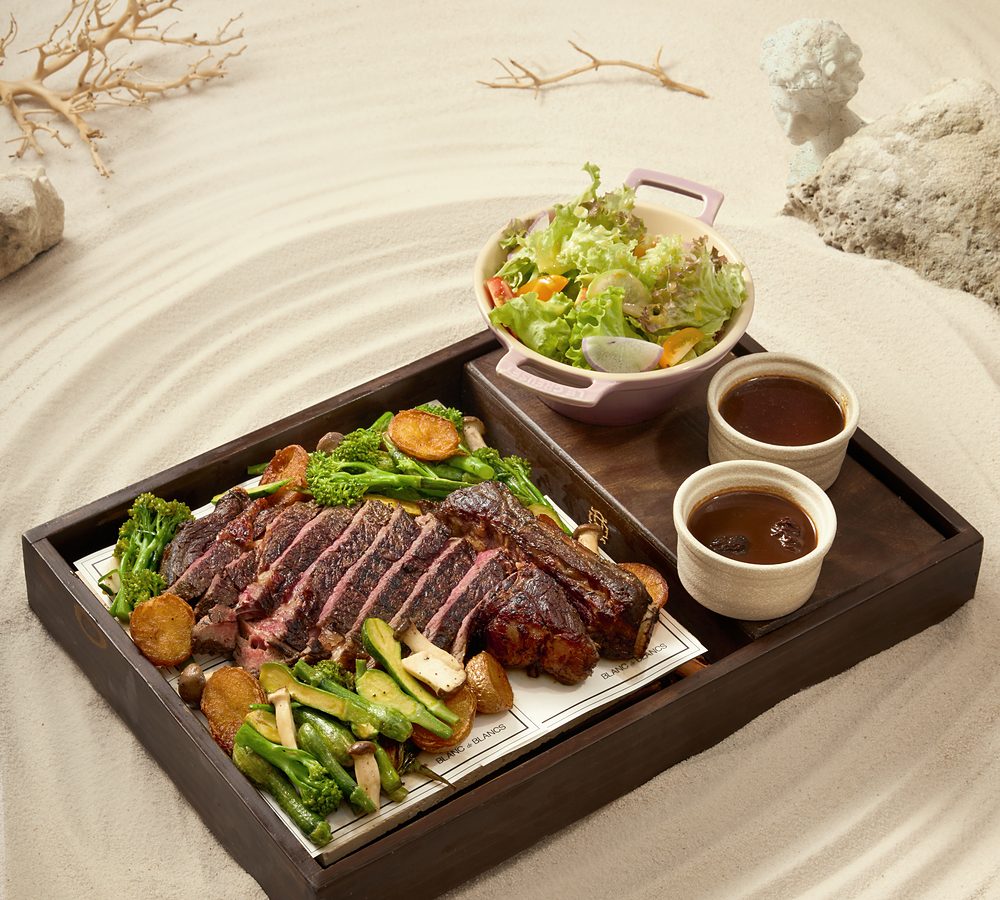 Sliced steak with vegetables, salad and sauces in a wooden tray